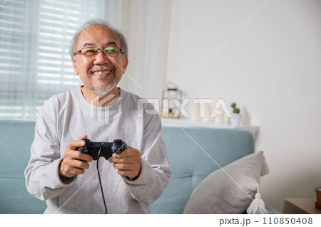 Funny retirement elderly smile sitting on sofa life gaming, lifestyle senior old man enjoying holding joystick playing video game at home, gamer mature man hands using game controller play videogame Funny retirement elderly smile sitting on sofa life gaming, lifestyle senior old man enjoying holding joystick playing video game at home, gamer mature man hands using game controller play videogame 110850408