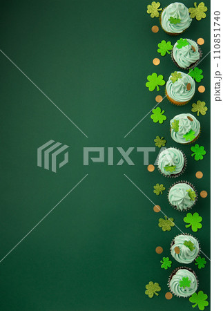 St. Patrick's Day vanilla and chocolate cupcakes with green frosting and  shiny clover decorations on green paper background. Irish holiday dessert concept. Top view, copy space. 110851740