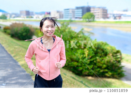 川沿いの道をジョギングする若い女性　ダイエット　ランニングウェア　トリミングアップ 110851859