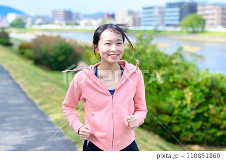 川沿いの道をジョギングする若い女性　ダイエット　ランニングウェア　トリミングアップ 110851860