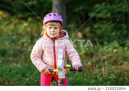Child riding balance bike. Kids on bicycle in sunny forest. Little girl enjoying to ride glider bike on warm day. Preschooler learning to balance on run bicycle in safe helmet. Sport activity 110852864
