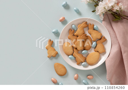 Homemade Easter bunnies shaped cookies and chocolate eggs on blue background. Top view. Space for text. Festive food and snacks. Greeting card. Homemade Easter bunnies shaped cookies and chocolate eggs on blue background. Top view. Space for text. Festive food and snacks. Greeting card. 110854260