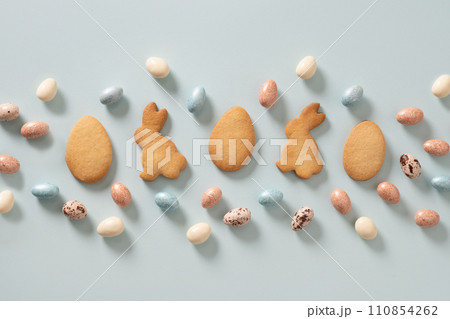 Easter glazed cookies shaped of bunny and chocolate sweets candy as eggs on blue background. View from above. Festive food and snacks. Greeting card. Easter glazed cookies shaped of bunny and chocolate sweets candy as eggs on blue background. View from above. Festive food and snacks. Greeting card. 110854262