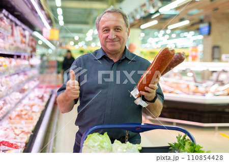 Mature man diligently choosing tasty sausage in supermarket 110854428