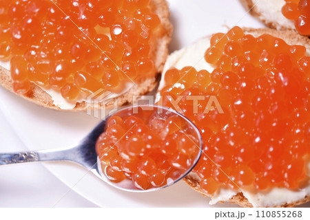 Red salmon caviar on bread and butter. A spoon with red caviar. Red salmon caviar on bread and butter. A spoon with red caviar. 110855268