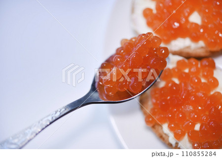 Red salmon caviar on bread and butter. A spoon with red caviar. Red salmon caviar on bread and butter. A spoon with red caviar. 110855284