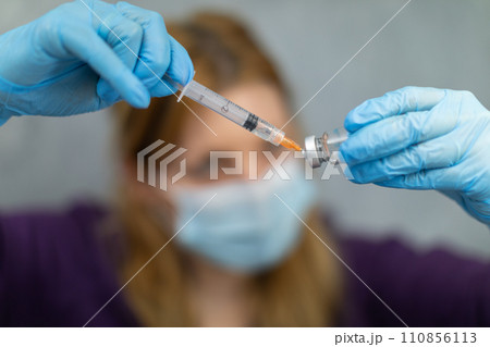 The nurse, wearing a surgical mask, scoops the therapeutic preparation into a syringe. The nurse, wearing a surgical mask, scoops the therapeutic preparation into a syringe. 110856113