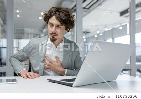 Professional young adult male office worker looking uneasy or stressed, with his hand on the chest, possibly experiencing burnout or health issues at work. Professional young adult male office worker looking uneasy or stressed, with his hand on the chest, possibly experiencing burnout or health issues at work. 110856206