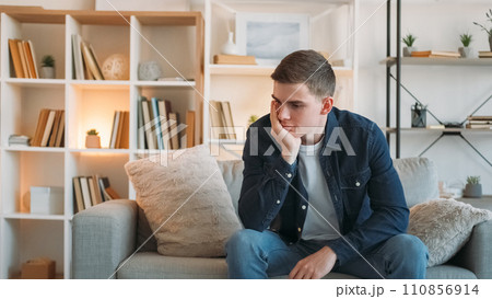 Frustration depression. Bad mood. Sad unhappy desperate pensive man with negative thoughts sitting on couch at home in living room copy space. Frustration depression. Bad mood. Sad unhappy desperate pensive man with negative thoughts sitting on couch at home in living room copy space. 110856914