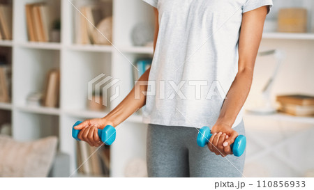 Dumbbells training. Home gym. Athletic fit healthy woman in activewear enjoying weights muscle physical aerobics workout indoors in living room. Dumbbells training. Home gym. Athletic fit healthy woman in activewear enjoying weights muscle physical aerobics workout indoors in living room. 110856933