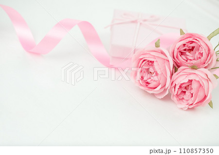 Three pink roses with ribbon and giftbox on the white table Three pink roses with ribbon and giftbox on the white table 110857350