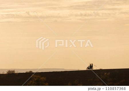 Silhouette of two men biker and a motorcycle on the road with sunset light background Silhouette of two men biker and a motorcycle on the road with sunset light background 110857368