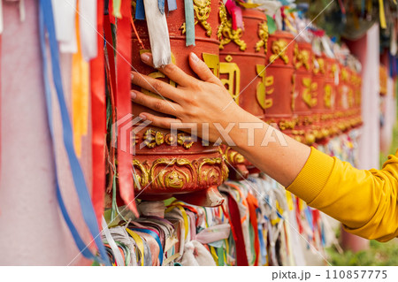 Person pilgrim female hand touching turning spinning Buddhist prayer wheel at Buddhist monastery. Prayer wheels in Buddhist stupa temple. Buddhism religion concept 110857775
