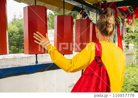 Person pilgrim woman touching turning spinning Buddhist prayer wheel at Buddhist monastery. Prayer wheels in Buddhist stupa temple. Buddhism religion concept 110857776