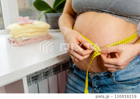 A pregnant woman measuring her belly with a yellow tape measure A pregnant woman measuring her belly with a yellow tape measure 110858219