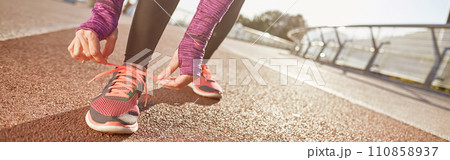 Being prepared. Cropped shot of active mature woman wearing sportswear tying her shoe laces while getting ready for running outdoors on a sunny day Being prepared. Cropped shot of active mature woman wearing sportswear tying her shoe laces while getting ready for running outdoors on a sunny day 110858937
