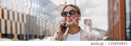 Stylish woman entrepreneur talking phone whiile standing on modern building background with coffee Stylish woman entrepreneur talking phone whiile standing on modern building background with coffee 110858941