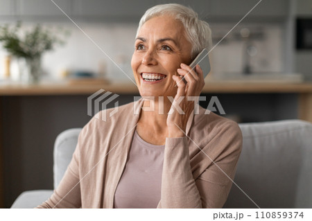 Positive beautiful mature lady having pleasant phone conversation at home 110859374