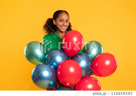 black teen girl posing with bunch of colorful balloons, studio 110859385