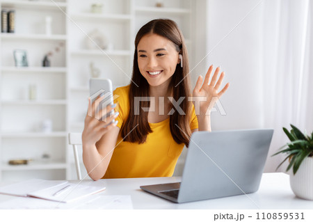 Asian Woman Making Video Call On Smartphone While Sitting In Home Office Asian Woman Making Video Call On Smartphone While Sitting In Home Office 110859531