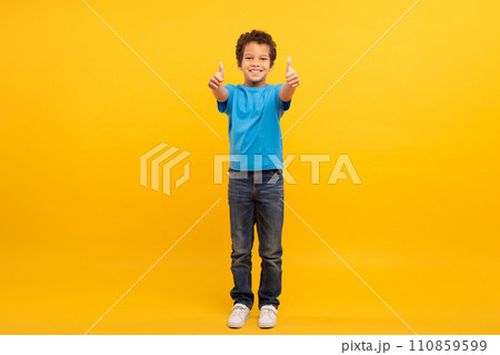 Boy in blue t-shirt giving thumbs up on sunny yellow background 110859599