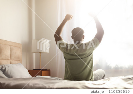 black guy sitting on bed indoor stretching body and arms 110859619