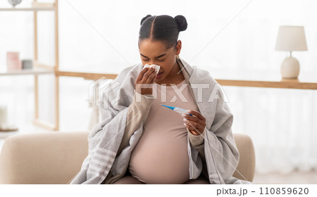 Sick pregnant black woman sneezing and checking body temperature 110859620