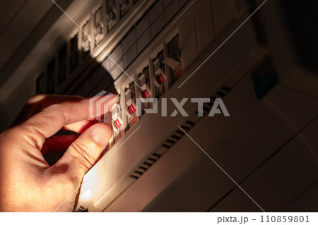 暗い部屋の中でブレーカーのスイッチを操作する 110859801