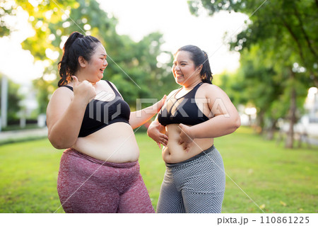 Two plus size woman share a moment during their workout in green park. 110861225