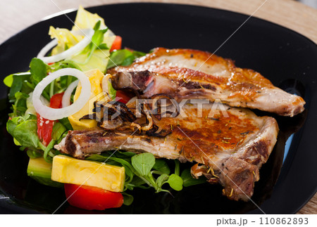 Frying pork loin at plate with avocado, tomatoes and corn salad 110862893