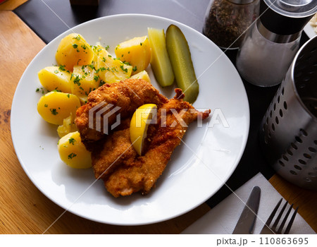 Parmesan breaded chicken schnitzel with potatoes and pickles 110863695