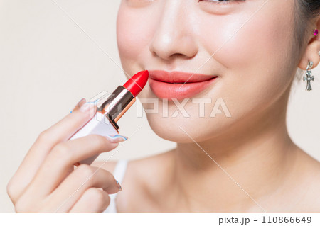 Young woman applying lipstick on beige 110866649