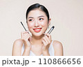 Beautiful asian young woman holding mascara and smiling on purple studio background, 110866656