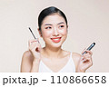 Beautiful asian young woman holding mascara and smiling on purple studio background, 110866658