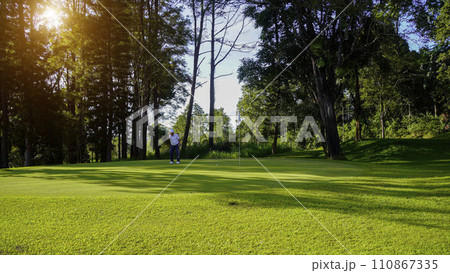 Golfer putting ball on the green golf, lens flare on sun set evening time. Golfer putting ball on the green golf, lens flare on sun set evening time. 110867335