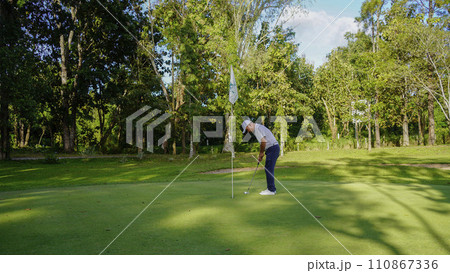 Golfer putting ball on the green golf, lens flare on sun set evening time. Golfer putting ball on the green golf, lens flare on sun set evening time. 110867336