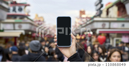 混雑する観光地とスマートフォンを持つ手 110868049