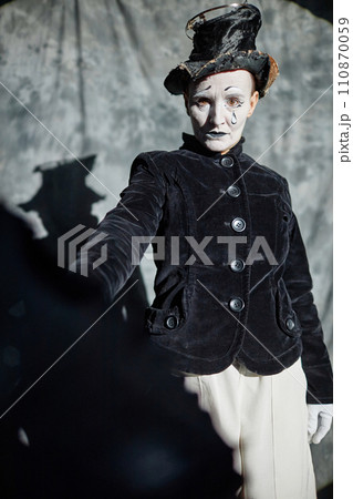 Dramatic portrait of female mime artist performing act on stage in spotlight and holding umbrella Dramatic portrait of female mime artist performing act on stage in spotlight and holding umbrella 110870059