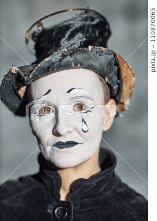 Vertical closeup portrait of female mime performer looking at camera with tear makeup 110870065