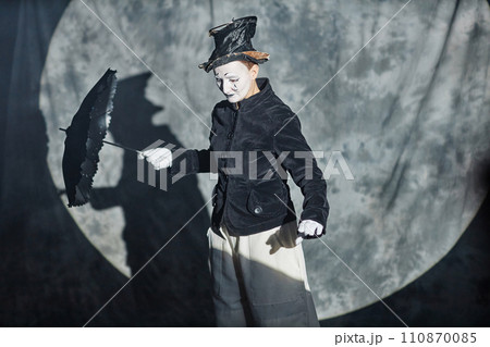 Waist up portrait of classic mime performer acting on stage in spotlight with umbrella, copy space 110870085