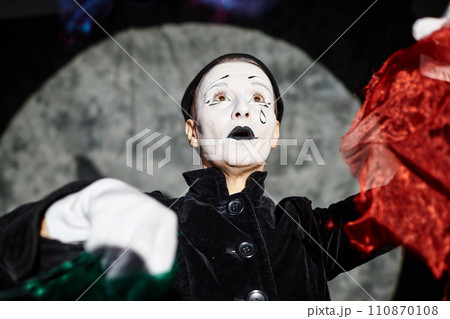Dramatic low angle portrait of mime artist performing on stage in spotlight and holding contrasting red cloth, copy space 110870108
