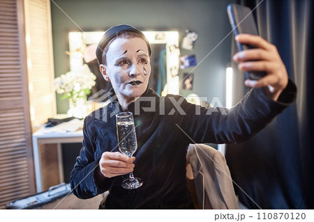 Waist up portrait of female mime performer taking selfie photo backstage in theater holding champagne glass, copy space Waist up portrait of female mime performer taking selfie photo backstage in theater holding champagne glass, copy space 110870120