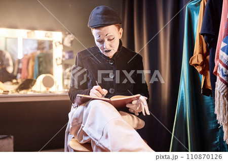 Dramatic portrait of mime performer preparing for show backstage and writing in notebook Dramatic portrait of mime performer preparing for show backstage and writing in notebook 110870126