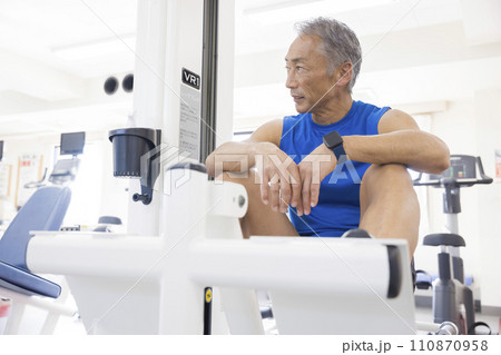スポーツジムの運動器具で休憩する中高年男性　 110870958