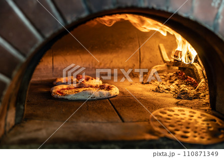 Traditional oven for baking pizza with burning wood and shovel. Several pizzas are baked in a brick oven Traditional oven for baking pizza with burning wood and shovel. Several pizzas are baked in a brick oven 110871349