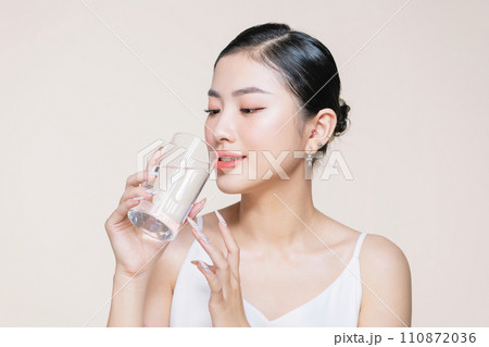 Young adult woman holds a glass of water in her hand near face 110872036