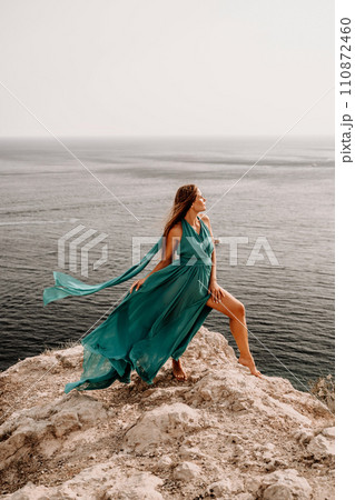Woman sea green dress. Side view a happy woman with long hair in a long mint dress posing on a beach with calm sea bokeh lights on sunny day. Girl on the nature on blue sky background. 110872460