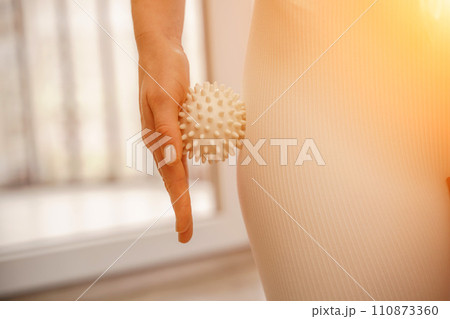 Athletic slim caucasian woman doing thigh self-massage with a massage ball indoors. Self-isolating massage 110873360