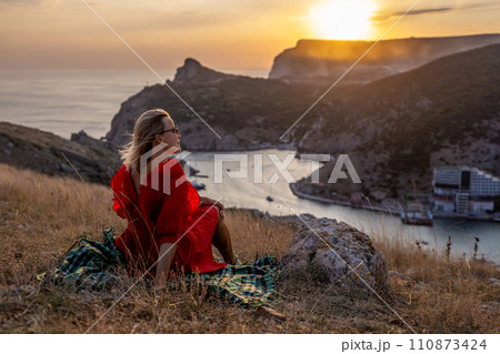 Woman sunset sea mountains. Happy woman siting with her back on the sunset in nature summer posing with mountains on sunset, silhouette. Woman in the mountains red dress, eco friendly, summer 110873424