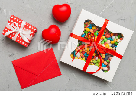 Red envelope with candy and gift box and Valentines hearts on colored background. Flat lay, top view. Romantic love letter for Holiday concept Red envelope with candy and gift box and Valentines hearts on colored background. Flat lay, top view. Romantic love letter for Holiday concept 110873784